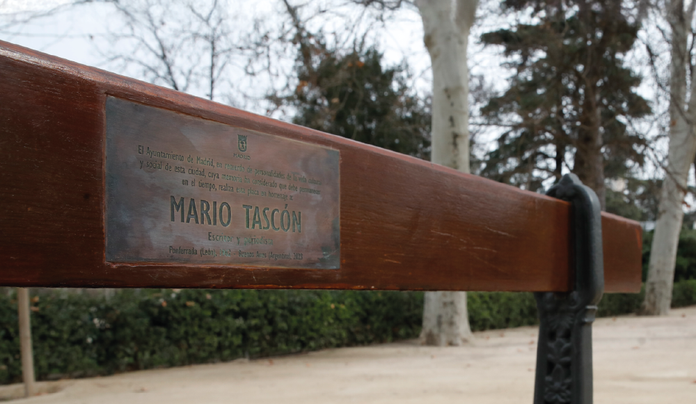 Parte superior del banco del Retiro donde pone una inscripción con el logo del ayuntamiento de Madrid que dice así: El Ayuntamiento de Madrid, en recuerdo de personalidades de la vida cultural y social de esta ciudad, cuya memoria ha considerado que debe permanenecer en el tiempo, realiza esta placa en homenaje a:
MARIO TASCÓN. Escritor y periodista. Ponferrada (León), 1962 - Buenos Aireas (Argentina), 2023.